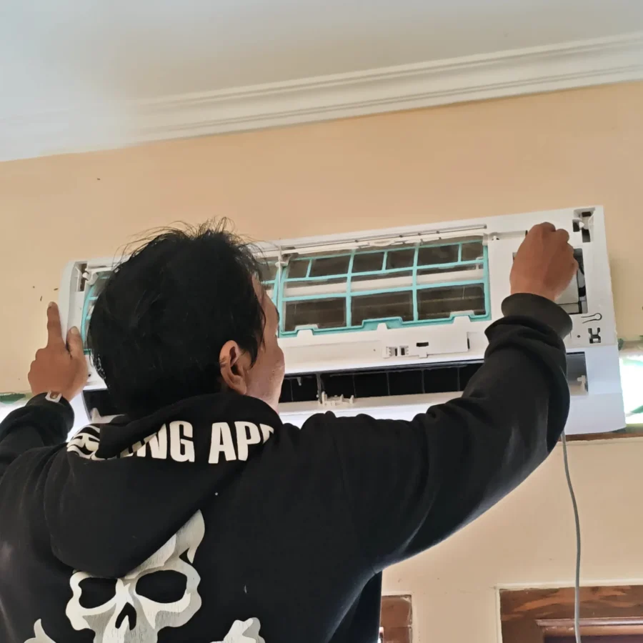 Teknisi sedang memasang kembali casing dan filter unit indoor AC yang sudah bersih setelah selesai dicuci